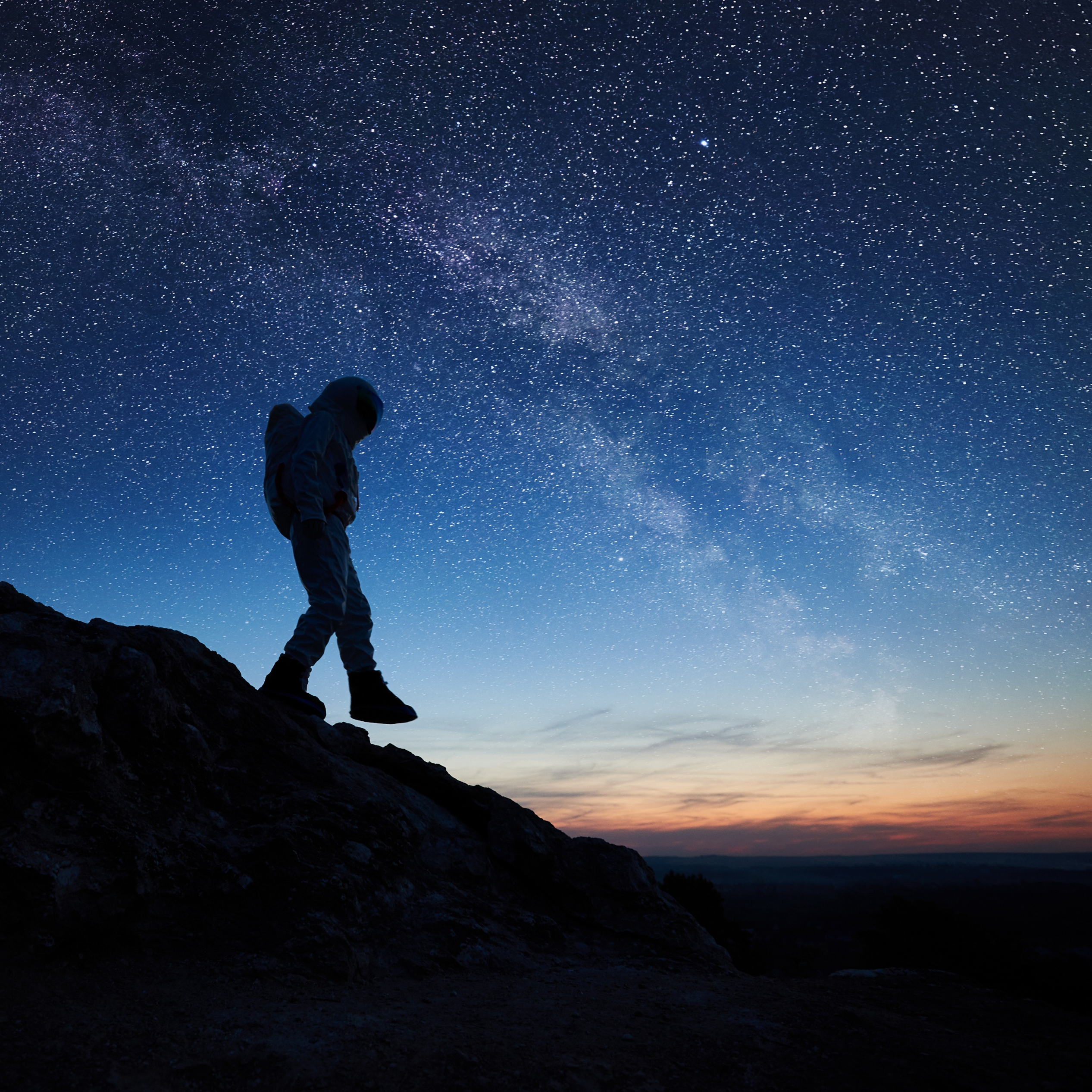 astronaut explorer stepping down off mountainous ridge, with starry sky in horizon