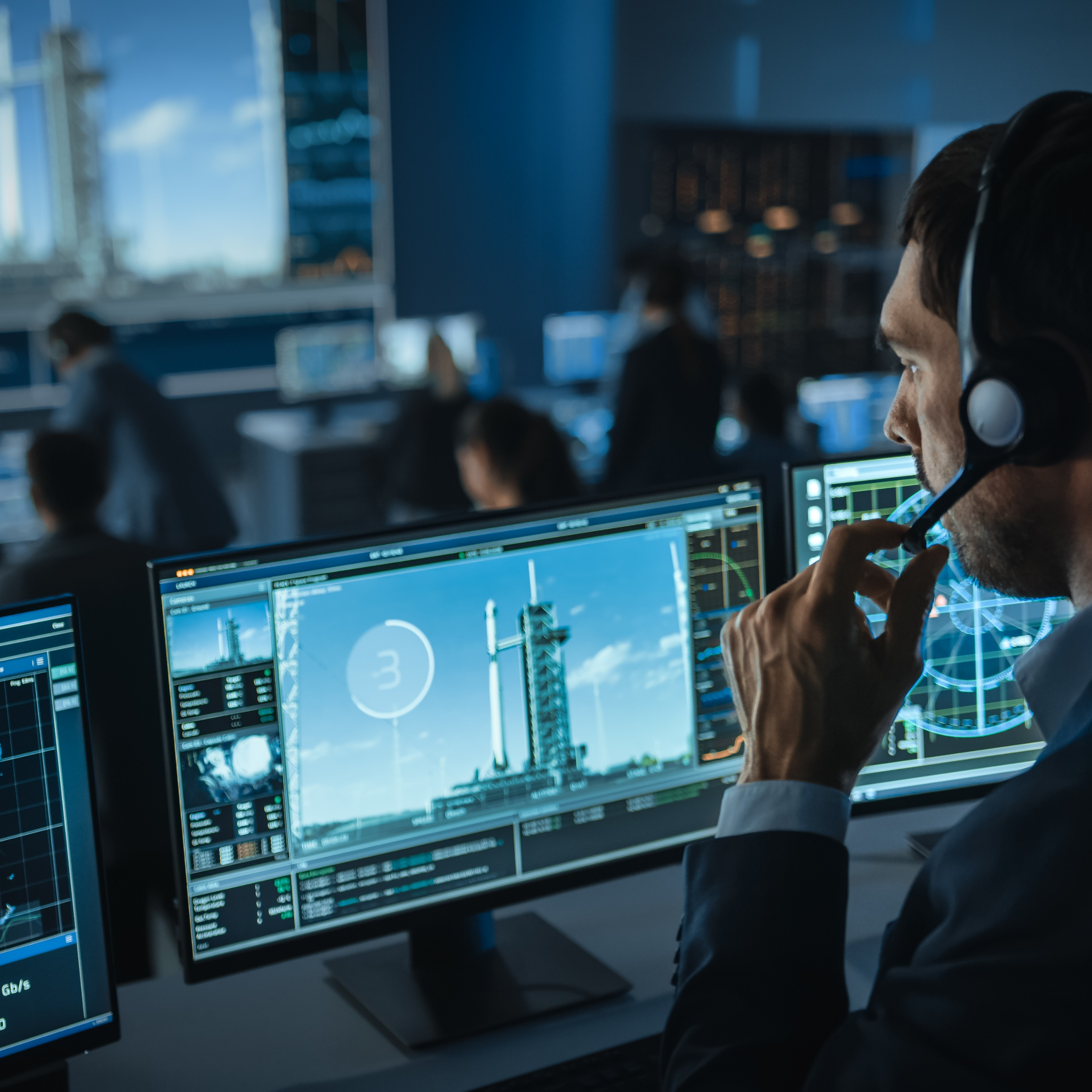 aerospace professional with headset in mission control room looking at monitors with launch vehicle on screen