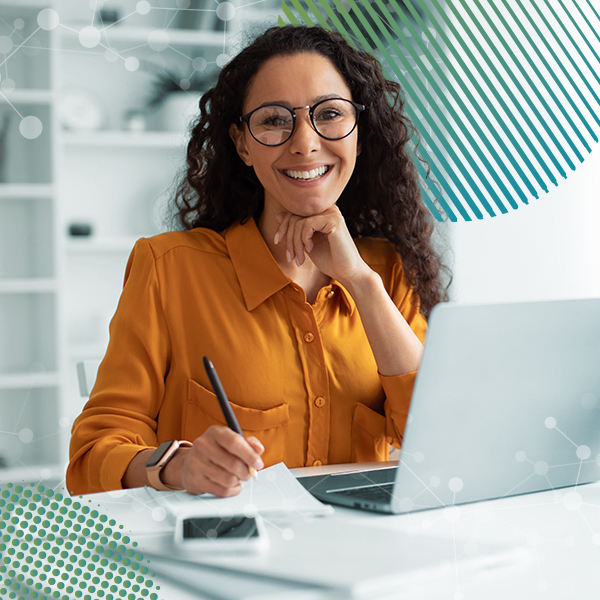 25236 Package A cheerful woman wearing glasses and a yellow blouse works at a desk with a laptop and pen in hand.